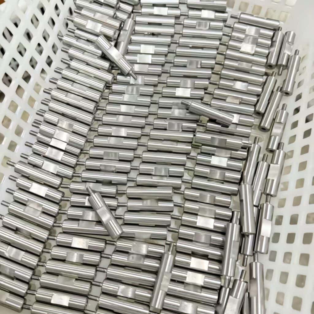 Orderly displayed stainless steel industrial workpieces arranged in white plastic bin for manufacturing and inspection