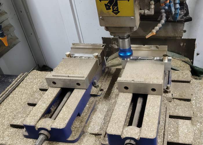 CNC milling machine cutting a brass workpiece, showing chips and vise fixtures during machining