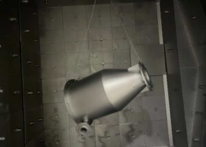 Large alloy steel part hanging inside a shot blasting chamber for heavy-duty surface preparation