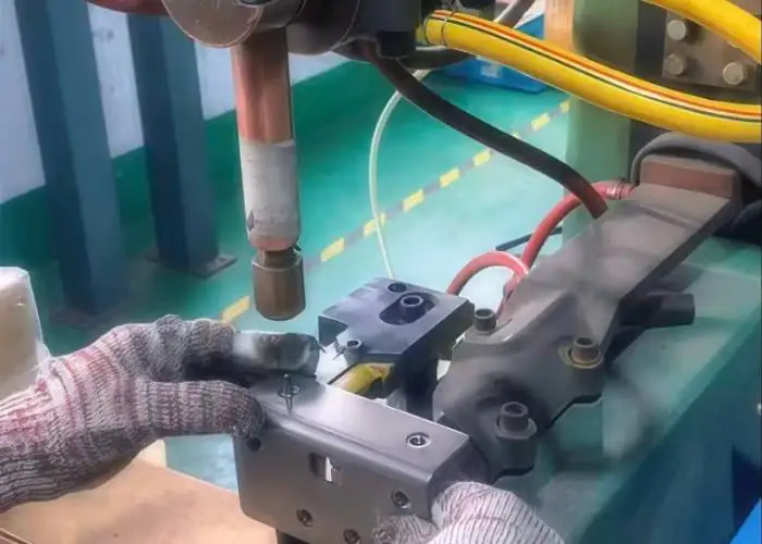 Worker operating a tack welding machine with welding tool for metal component assembly