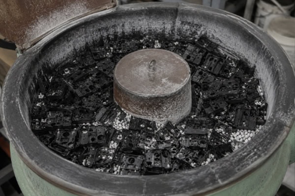 Vibratory deburring of plastic parts processed by CNC machining is typically performed in conjunction with rollers or rotary equipment using abrasive materials on-site.