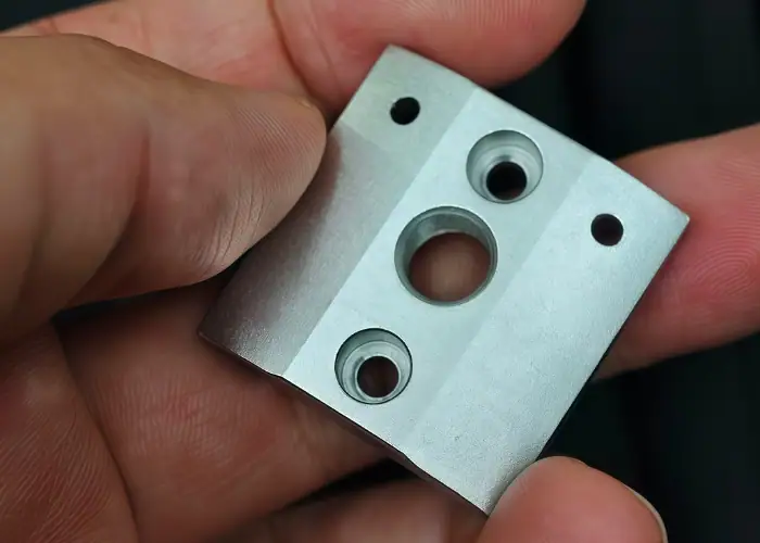 Bead-blasted aluminum square mounting block with multiple holes and counterbores produced by precision CNC machining.