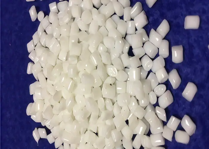 Off-white PBT plastic resin pellets displayed as raw material for injection molding and engineering plastic part production.