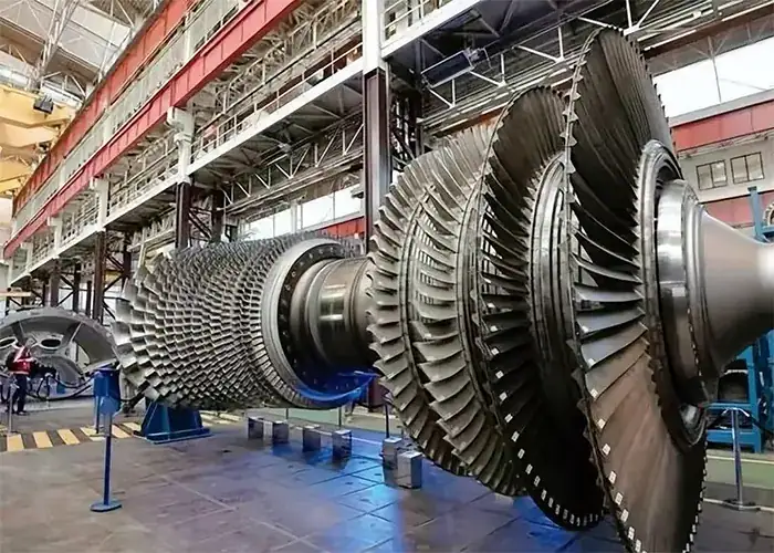 Large turbine rotor with multiple rows of blades displayed in a workshop